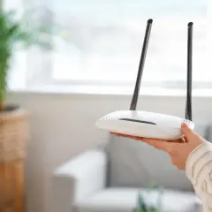 Dłoń trzyma biały router Wi-Fi z dwiema antenami. Może to być pomocne, gdy zastanawiasz się, jak zresetować urządzenie.