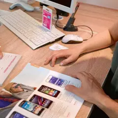 Klienci przeglądają ofertę smartfonów T-Mobile. Na biurku klawiatura, myszka i dokumenty.