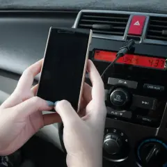 Ręce trzymają telefon, który jest podłączony do radia samochodowego. Właśnie pokazano, jak połączyć telefon z systemem audio auta.
