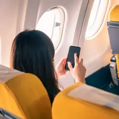 Kobieta w samolocie korzysta z telefonu, pamiętając o włączeniu trybu samolotowego.