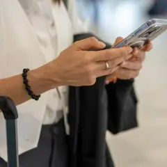 Kobieta z telefonem w dłoni, obok walizki. Sprawdza informacje o wyłączeniu 3G Plus, przygotowując się do podróży.