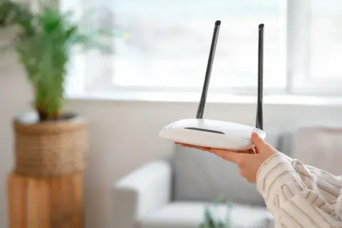 Dłoń trzyma biały router Wi-Fi z dwiema antenami. Może to być pomocne, gdy zastanawiasz się, jak zresetować urządzenie.
