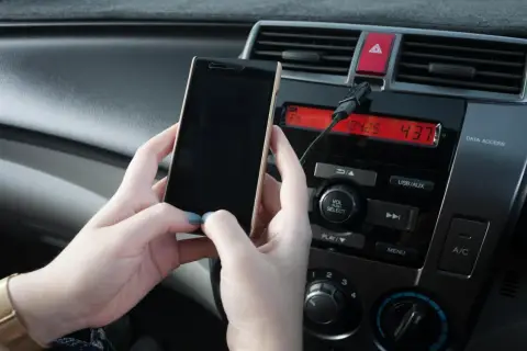 Ręce trzymają telefon, który jest podłączony do radia samochodowego. Właśnie pokazano, jak połączyć telefon z systemem audio auta.