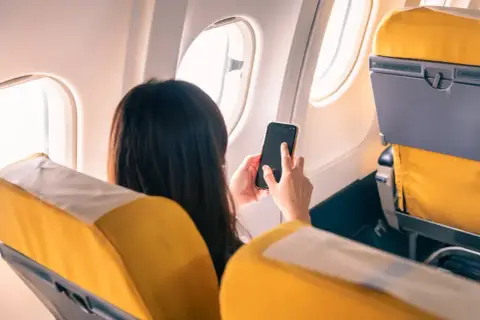 Kobieta w samolocie korzysta z telefonu, pamiętając o włączeniu trybu samolotowego.